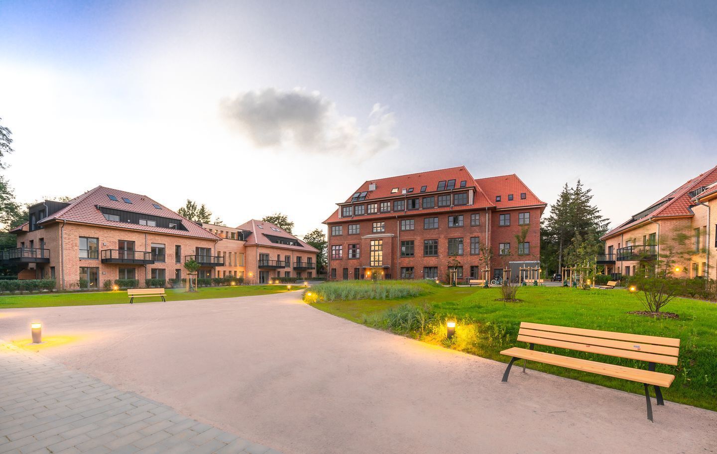 Ein Wohnhauskomplex mit mehreren Ziegelgebäuden, einem zentralen Innenhof mit einer Bank und einem gepflegten Rasen.