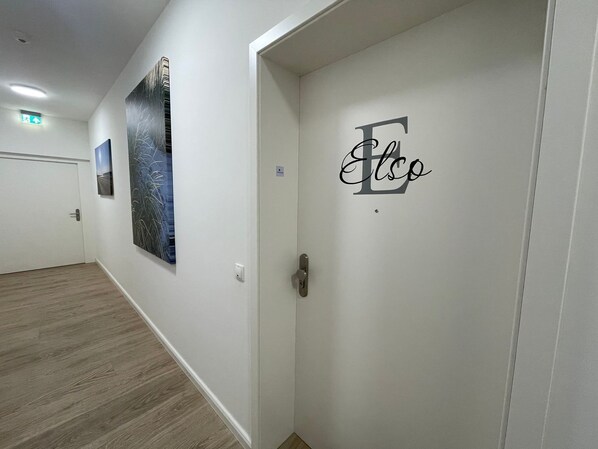 A hallway with a white door labeled "Elso," a framed artwork on the wall, and a light switch.