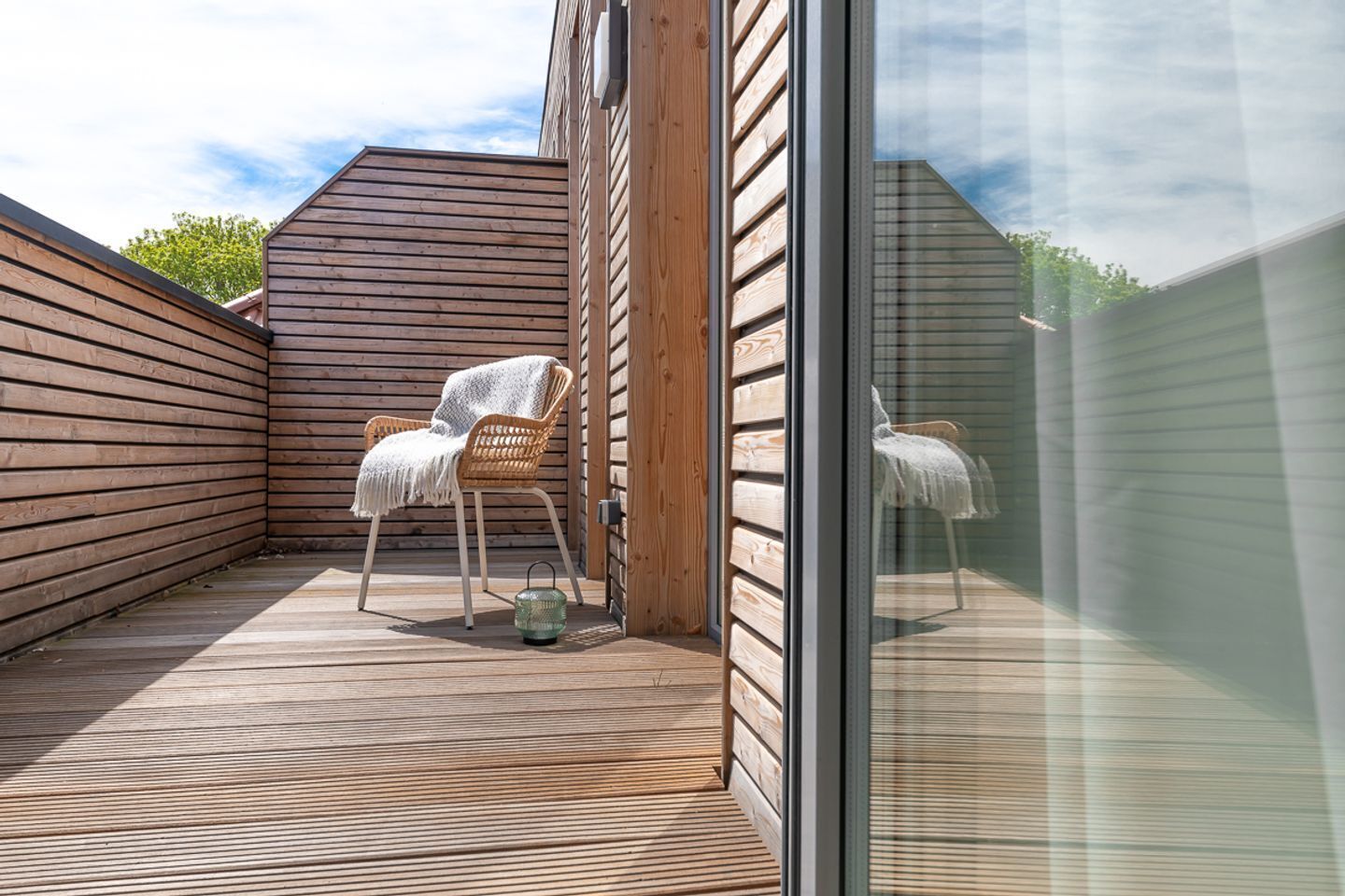 Eine Holzterrasse mit zwei Korbstühlen, einer mit einer Decke.
