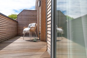 Una terraza de madera con dos sillas de mimbre, una con una manta.