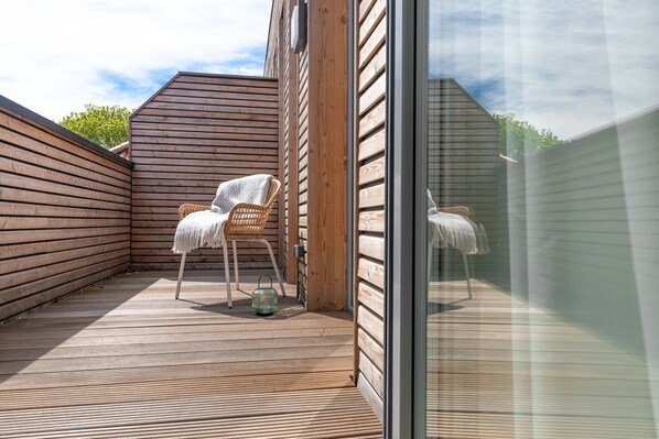 Eine Holzterrasse mit zwei Korbstühlen, einer mit einer Decke.