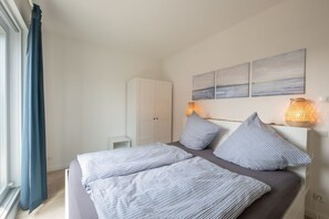 Quarto com cama, duas mesas de cabeceira, guarda-roupa e janela com cortinas.