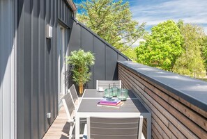 Ein Balkon mit Tisch und Stühlen, einem Blumentopf und Blick auf Bäume.