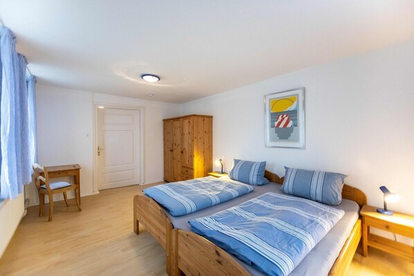A bedroom with two beds, a wooden wardrobe, a chair, and a door.