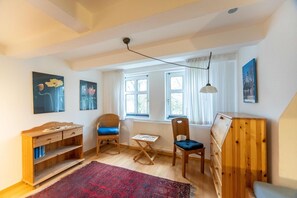 A cozy room with a wooden desk, two chairs, a radiator, and a window with curtains.