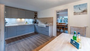 Una cucina moderna con mobili grigi, un piano di lavoro in legno e un lavello incassato. Si intravede un'area pranzo attraverso un'apertura.