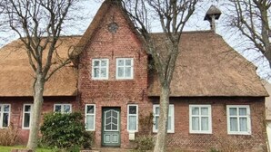 Una casa tradizionale in mattoni con tetto di paglia, un ingresso centrale con porta verde e un vialetto in mattoni che conduce al davanti.