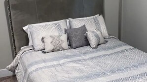 A bed with a patterned bedspread and pillows, a headboard, and a carpeted floor. - Private oasis (Charlotte)