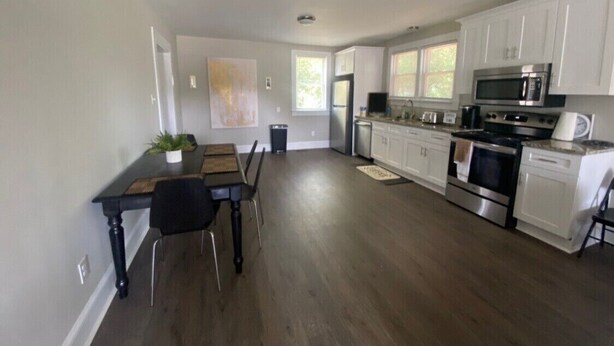 A modern kitchen with white cabinets, stainless steel appliances, and a dining area with a wooden table and chairs. - Private oasis (Charlotte)