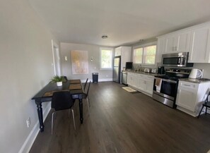 A modern kitchen with white cabinets, stainless steel appliances, and a dining area with a wooden table and chairs. - Private oasis (Charlotte)