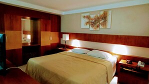 Een hotelkamer met een groot bed, een houten hoofdeinde, een bureau met een lamp, een telefoon en een spiegel.