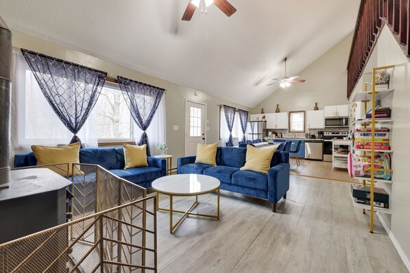 A spacious living area with blue sofas, a round coffee table, and a kitchen in the background.