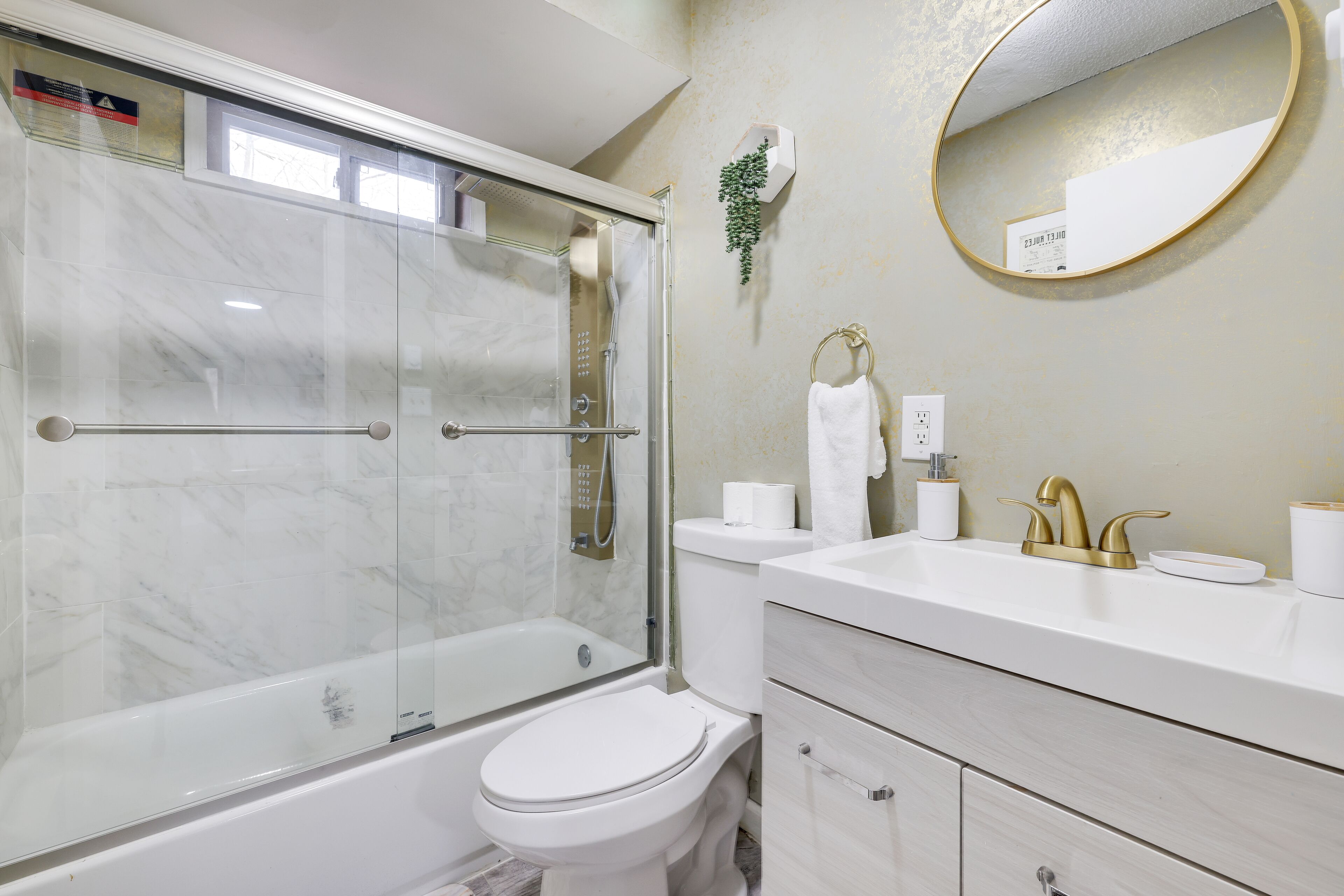 A modern bathroom with a glass-enclosed shower, a white toilet, and a vanity with a gold faucet.