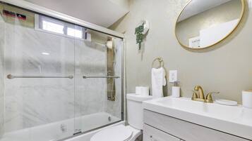 A modern bathroom with a glass-enclosed shower, a white toilet, and a vanity with a gold faucet.