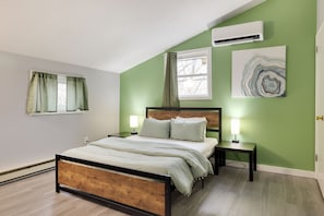 A bedroom with a wooden bed, green walls, a window with curtains, and a wall-mounted air conditioner.