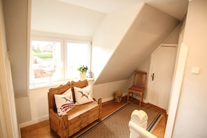 Une chambre confortable située dans les combles, avec un banc en bois, une chaise et une fenêtre donnant sur l’extérieur.