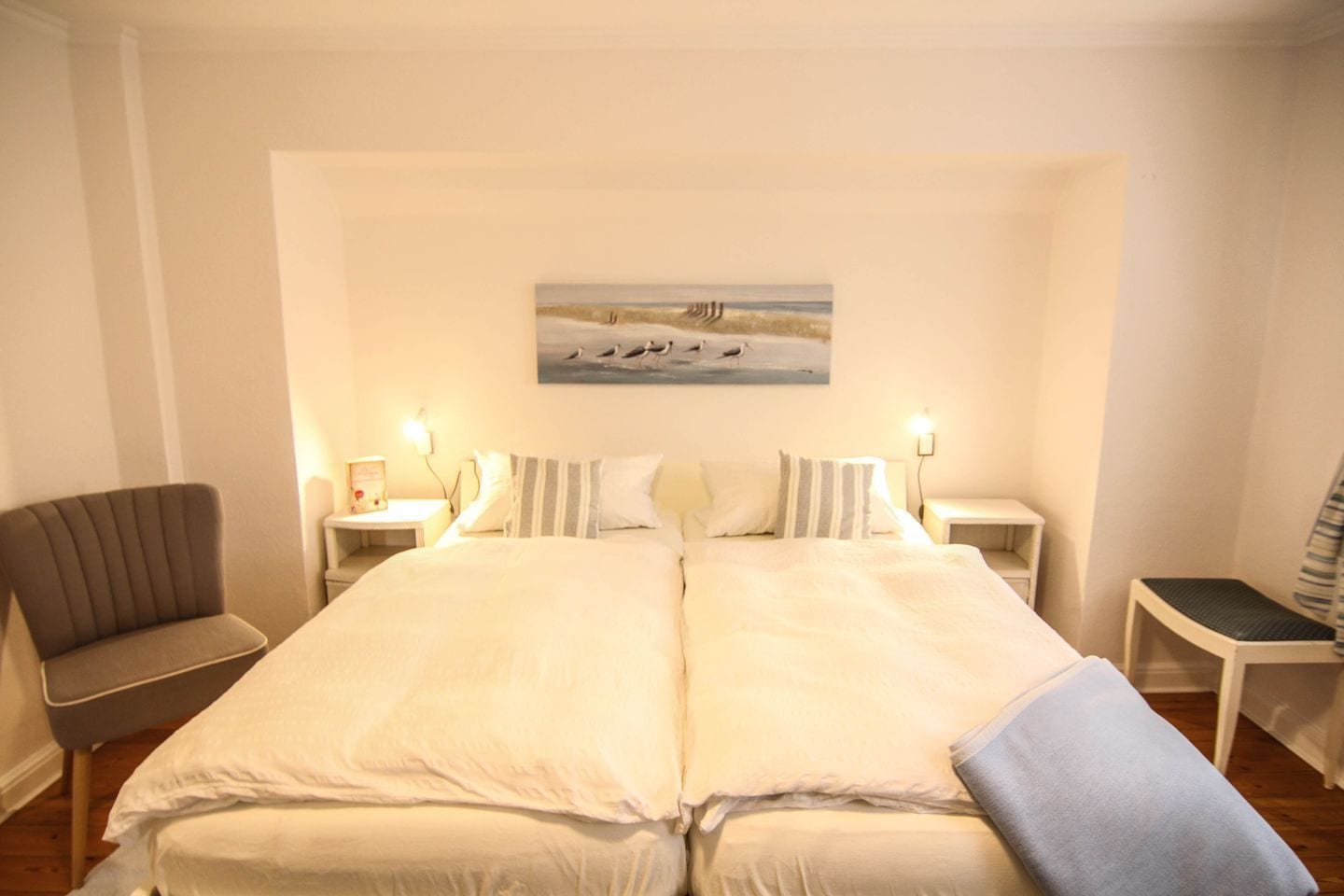 A hotel room with a large bed, two bedside tables, a chair, and a painting on the wall.