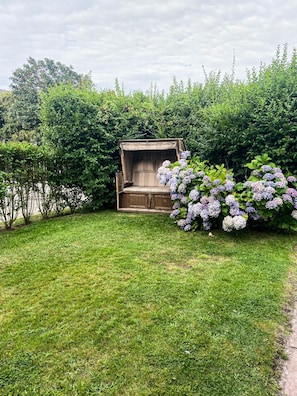 Un jardin avec un banc en bois et un groupe d’arbustes d’hortensias aux fleurs violettes.