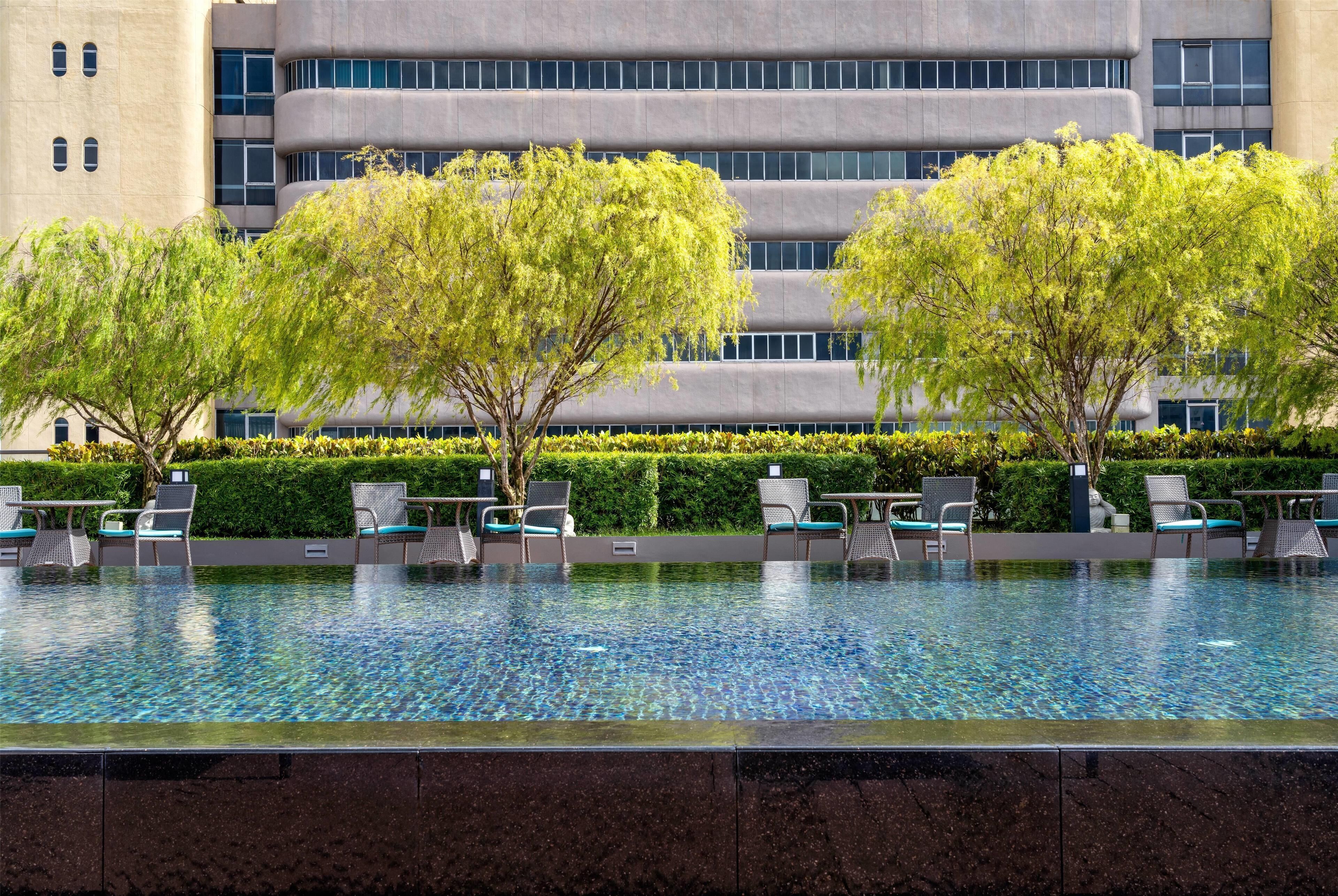 A modern hotel pool area with a clear view of the building's exterior, including a multi-story structure with a flat roof and large windows.