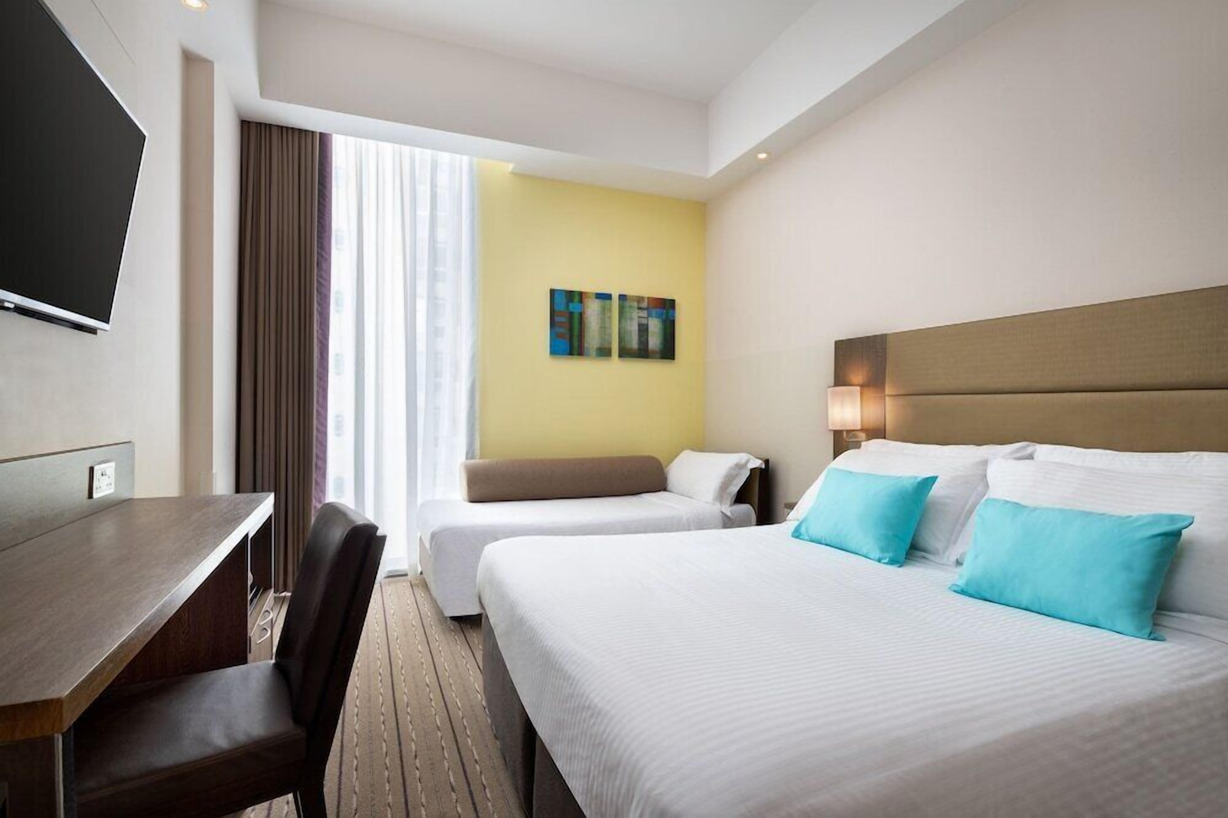 A hotel room with a bed, a desk, a chair, a television, and a window with curtains.