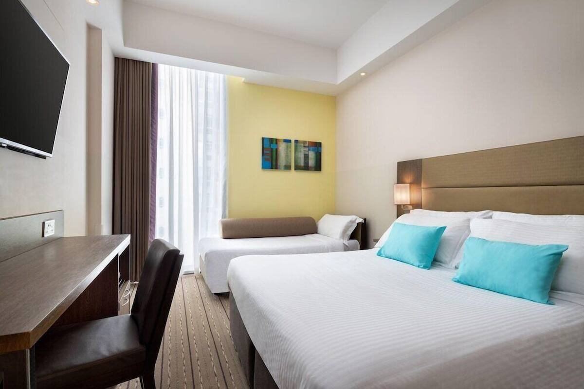 A hotel room with a bed, a desk, a chair, a television, and a window with curtains.