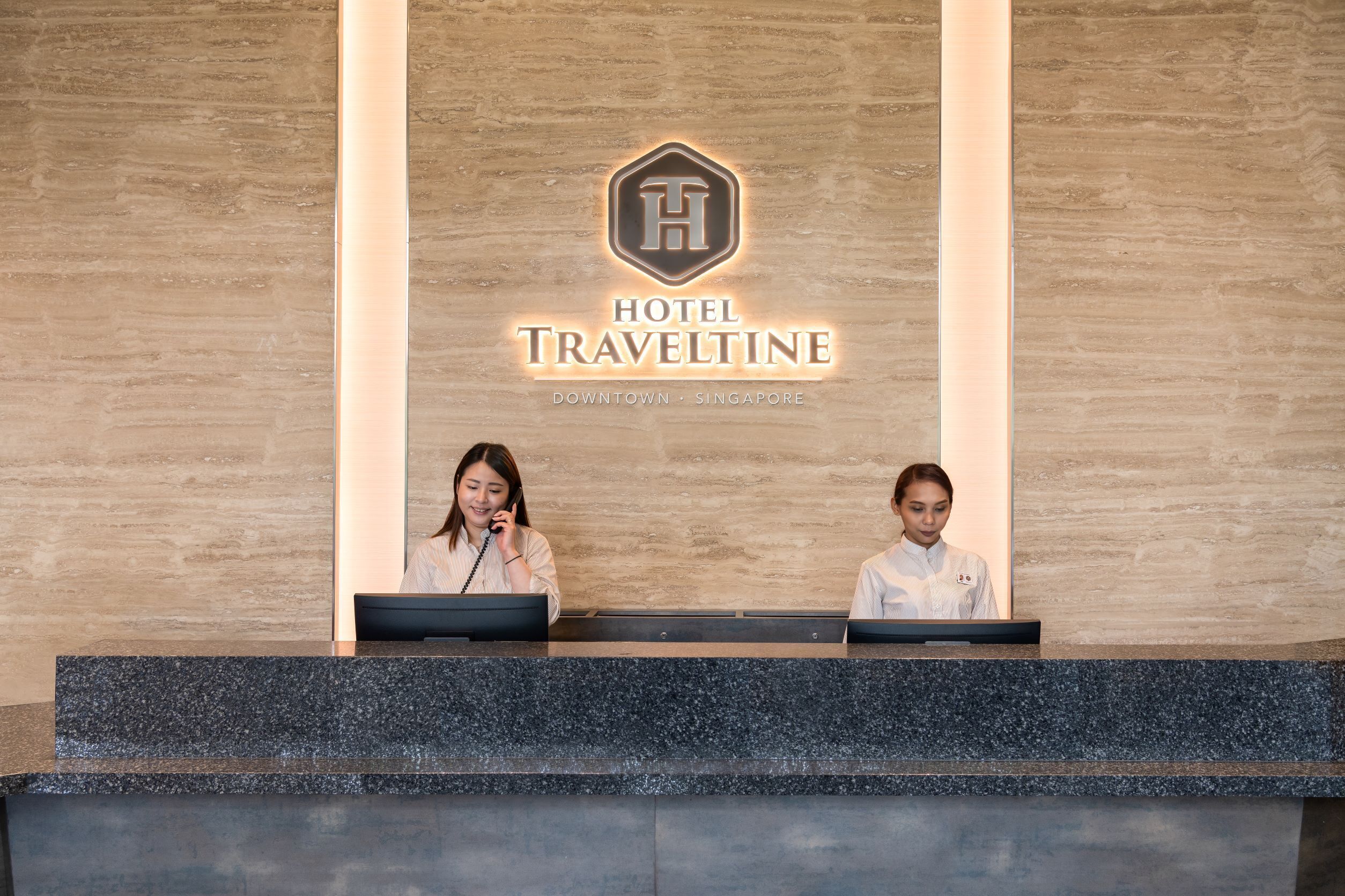 A reception desk with two staff members at a Hotel Traveltine in Downtown Singapore.