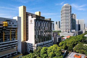 Um edifício moderno e urbano com fachada singular, rodeado por outros edifícios altos e áreas verdes.