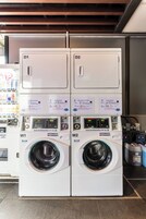 Two white automatic detergent machines with digital displays and control panels, located in a commercial setting with a tiled floor.