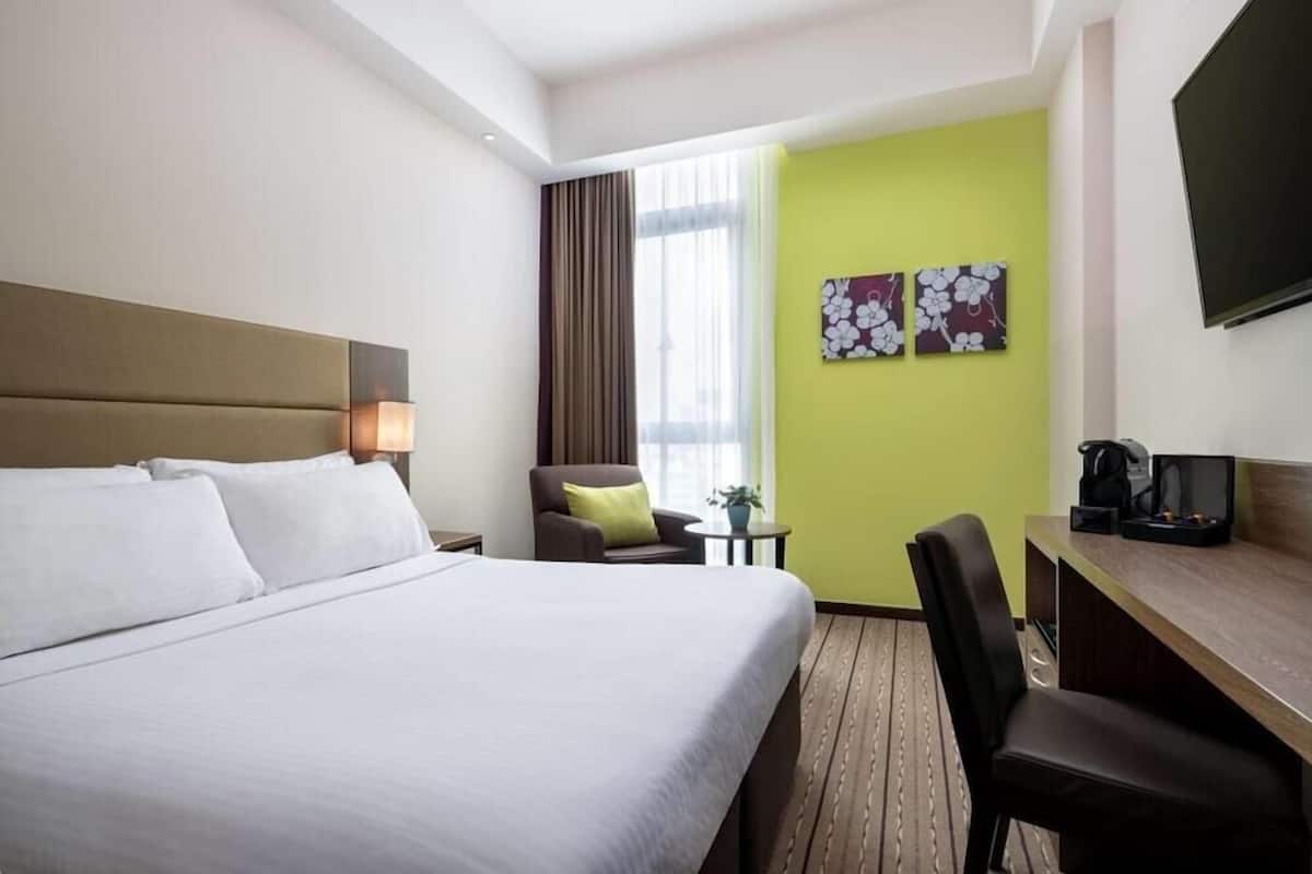 Habitación de hotel con cama, escritorio, silla, televisión y ventana con cortinas.