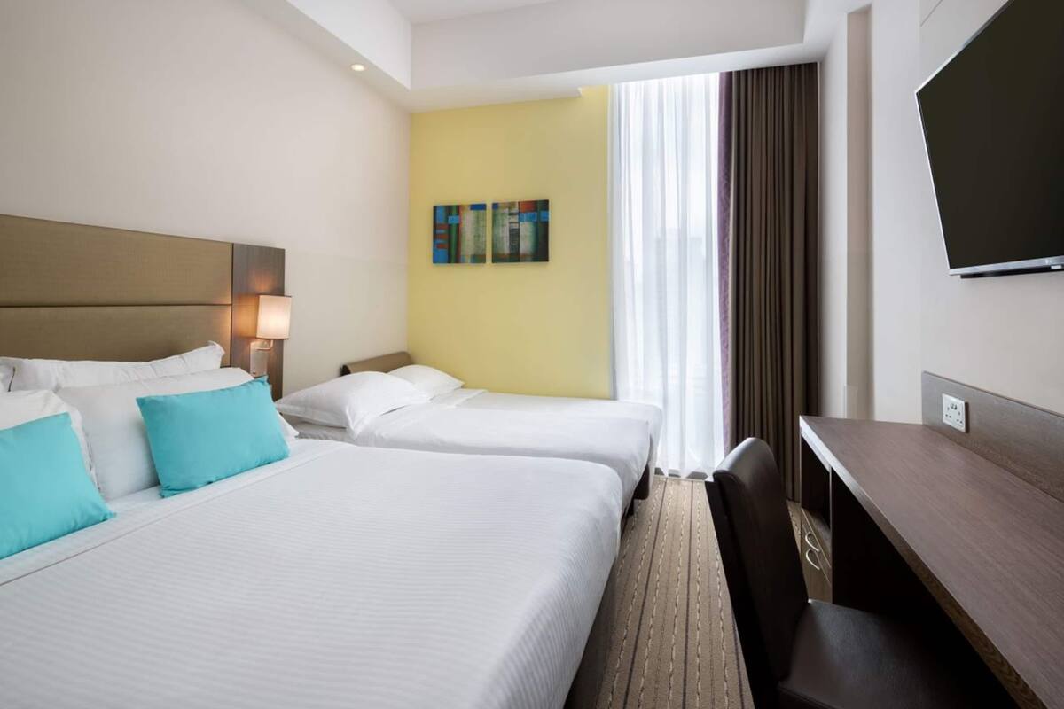 A hotel room with two beds, a desk, a chair, a TV, and a window with curtains.