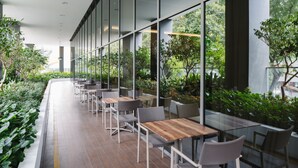 A modern outdoor dining area with wooden tables and chairs, surrounded by glass walls and greenery. - Hotel Traveltine Downtown Singapore, Trademark Collection by Wyndham (Singapore)