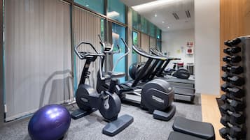 Une salle de sport équipée de tapis de course, de vélos elliptiques, d’un vélo d’appartement, d’un ballon d’exercice violet et d’un porte-haltères.