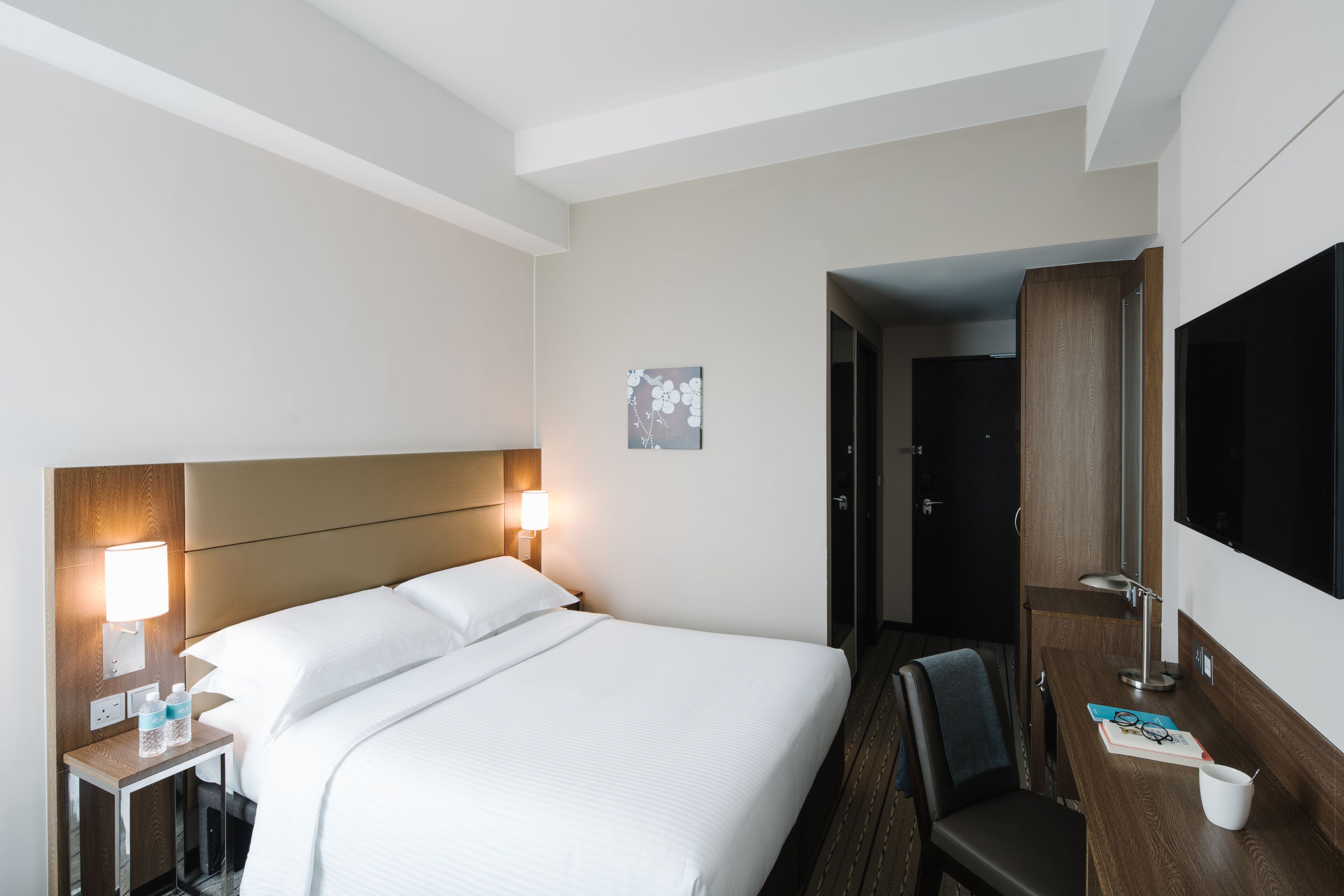 Habitación de hotel con una cama grande, lámparas de noche, un escritorio con silla y un televisor.
