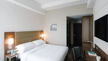Habitación de hotel con una cama grande, lámparas de noche, un escritorio con silla y un televisor.