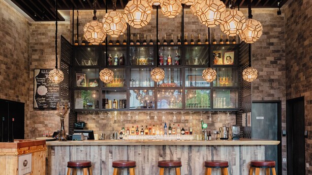 A bar with a wooden counter, multiple stools, and hanging hexagonal light fixtures. - Hotel Traveltine Downtown Singapore, Trademark Collection by Wyndham (Singapore)