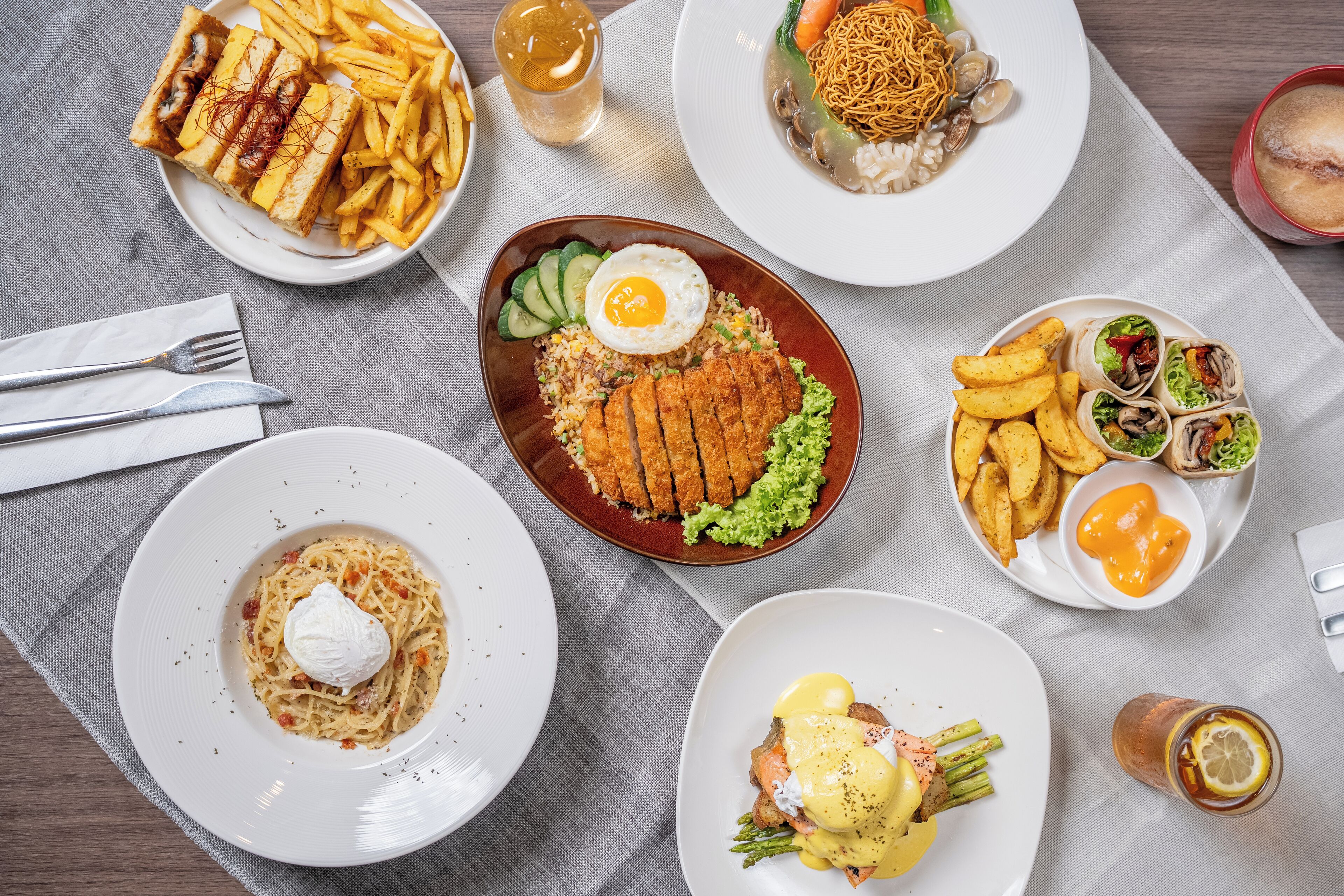 Verschiedene Gerichte, darunter Pasta, gebratenen Reis und Sandwiches, sind auf einem Tisch mit Tischdecke angerichtet.