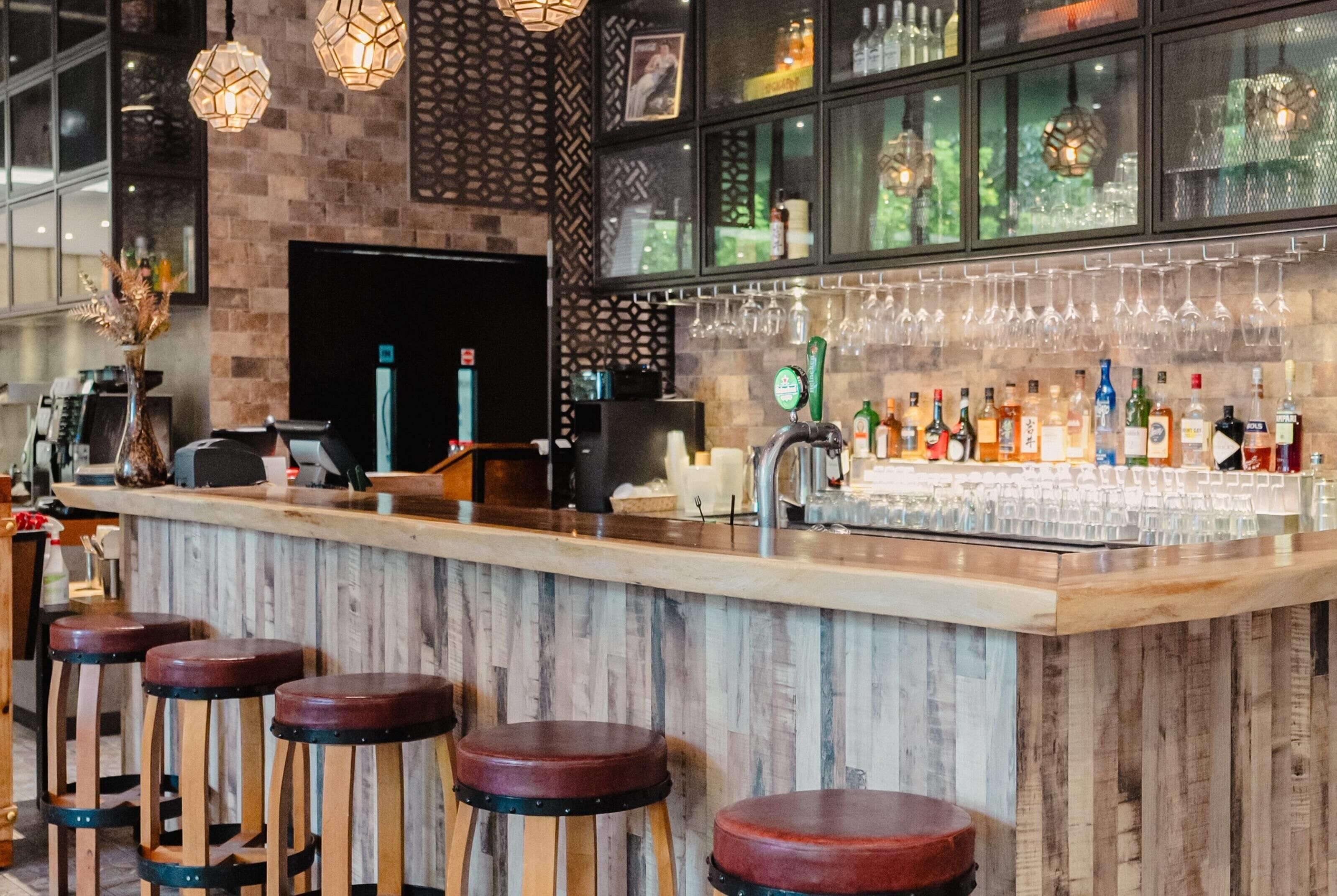 Un área de bar con taburetes de madera, una barra y varias botellas y vasos.