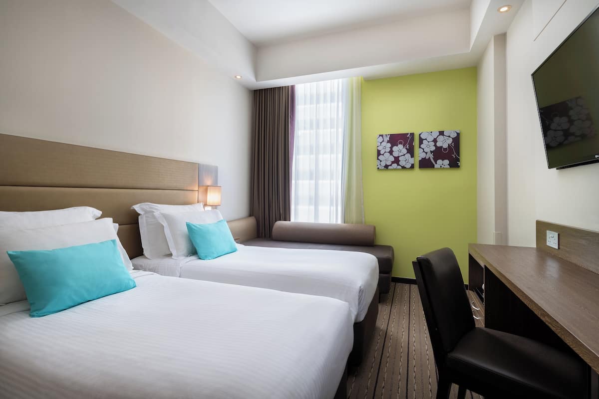 A hotel room with two beds, a desk, and a TV.
