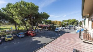 Un parking avec plusieurs voitures, un bâtiment avec un toit rouge et un grand arbre.