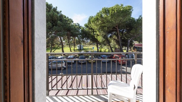 Un balcon donnant sur des voitures garées et des arbres.
