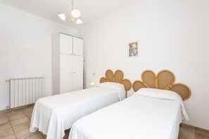 A room with two single beds, a white wardrobe, a radiator, and a wall-mounted light fixture.