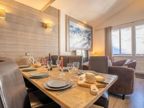 A dining area with a wooden table set for four, surrounded by leather chairs. A painting of mountains is on the wall, and there is a window with curtains. - Rond Point des Pistes (Val Claret) by Interhome (Tignes)