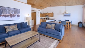 A spacious living area with a large sofa set, a wooden coffee table, and a kitchen in the background.