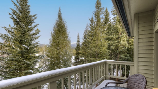 A balcony with a view of snow-covered trees and mountains.