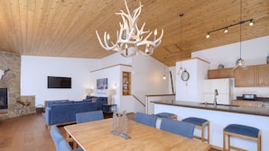 A spacious living area with a wooden dining table, blue upholstered chairs, a stone fireplace, a blue sofa, and a kitchen with wooden cabinets and a built-in microwave.