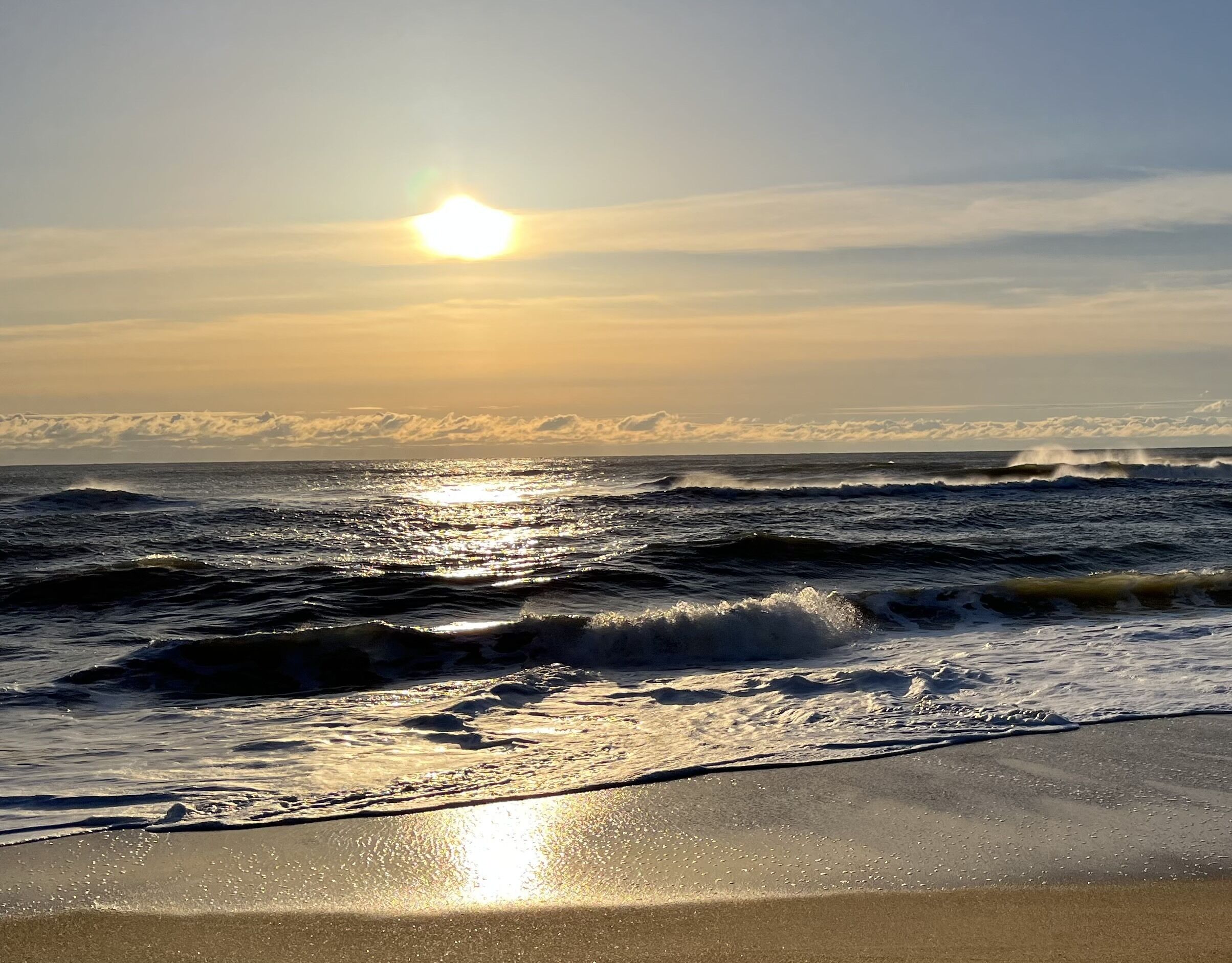 A beach with waves and the sun reflecting on the water.