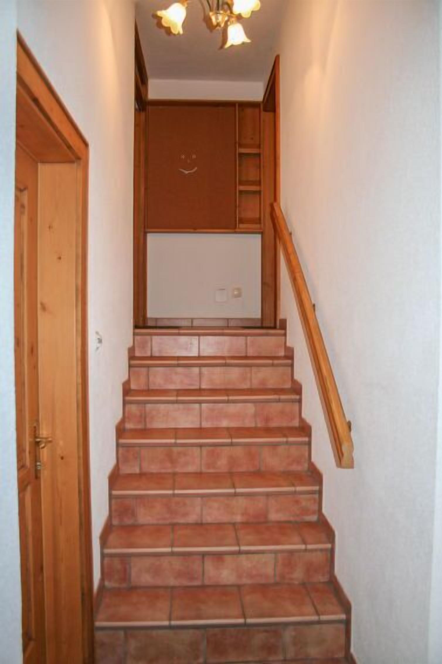 Un escalier avec des rampes en bois et un sol carrelé menant à un palier où se trouve un tableau blanc.
