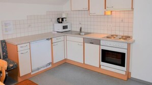 Een compacte keuken met witte kastjes, een magnetron, een koffiezetapparaat, een spoelbak en een fornuis.