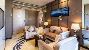 Une chambre d’hôtel moderne, équipée d’un canapé, de fauteuils, d’une table basse et d’un téléviseur fixé au mur.