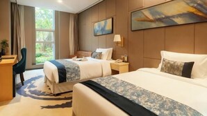 Une chambre d’hôtel avec deux lits, un bureau, une chaise, une fenêtre avec des rideaux et des œuvres d’art accrochées aux murs.